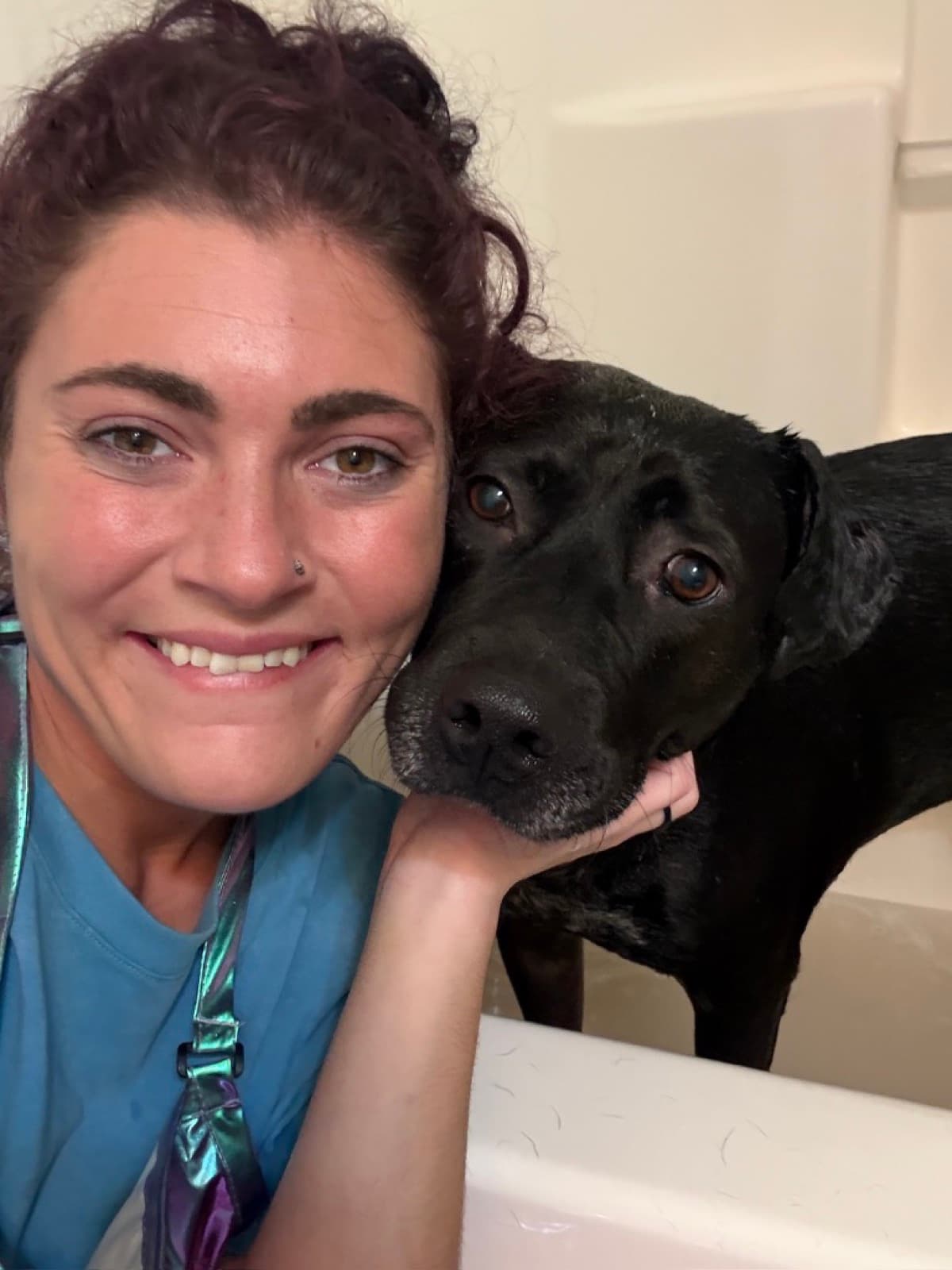 Jamie smiling beside a black dog in the tub