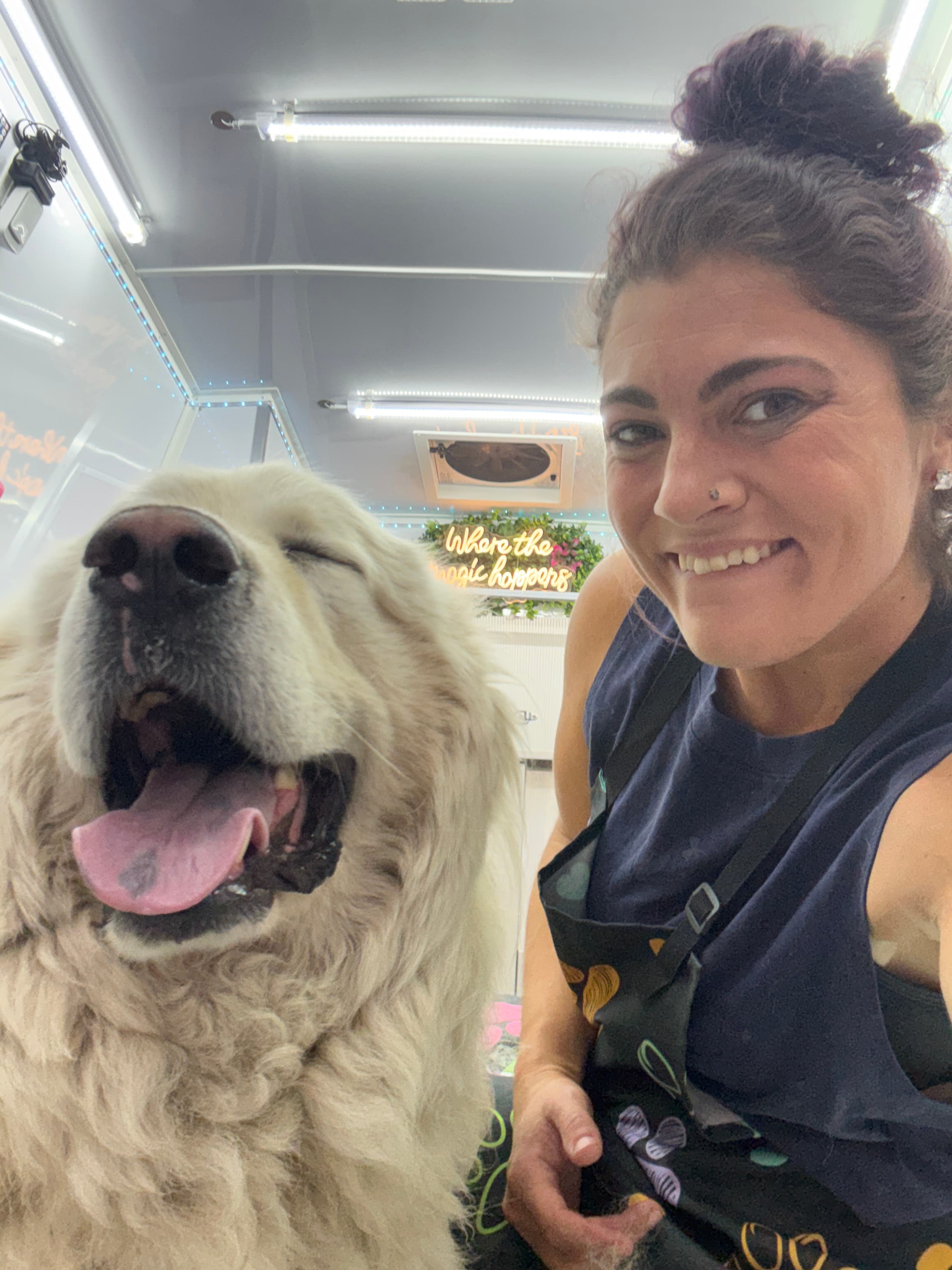 Jamie smiling beside a large double-coated dog in the mobile grooming spa