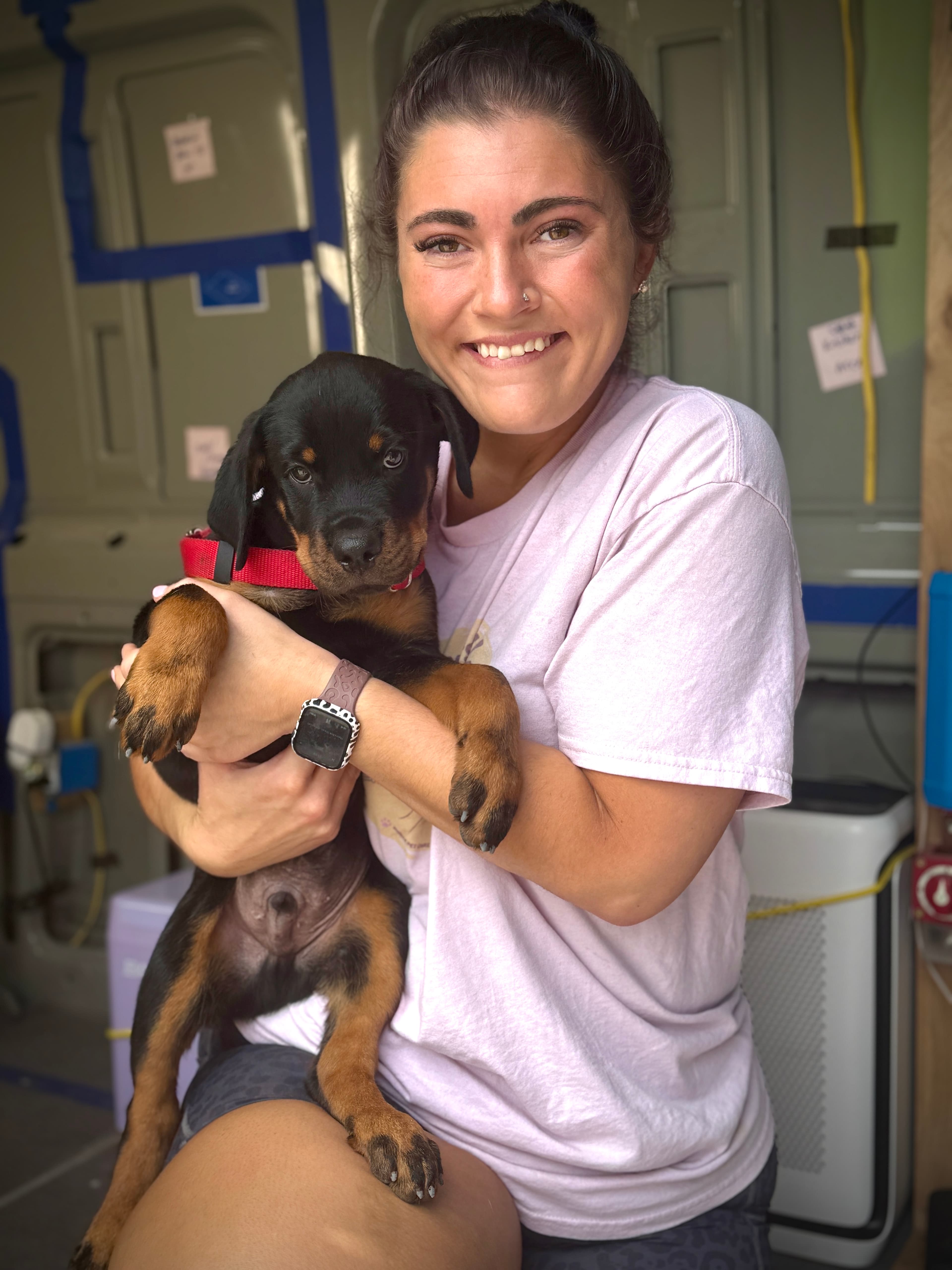 Jamie smiling while holding a puppy in the mobile grooming spa